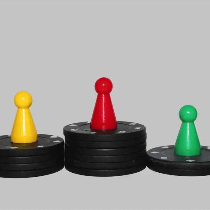 Drei bunte Spielfiguren stehen auf Stapeln schwarzer Pokerchips wie auf einem Siegertreppchen.