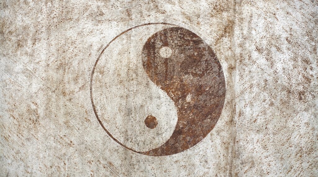 Ein verrostetes Yin-Yang-Symbol auf einer hellen, verwitterten Metalloberfläche.