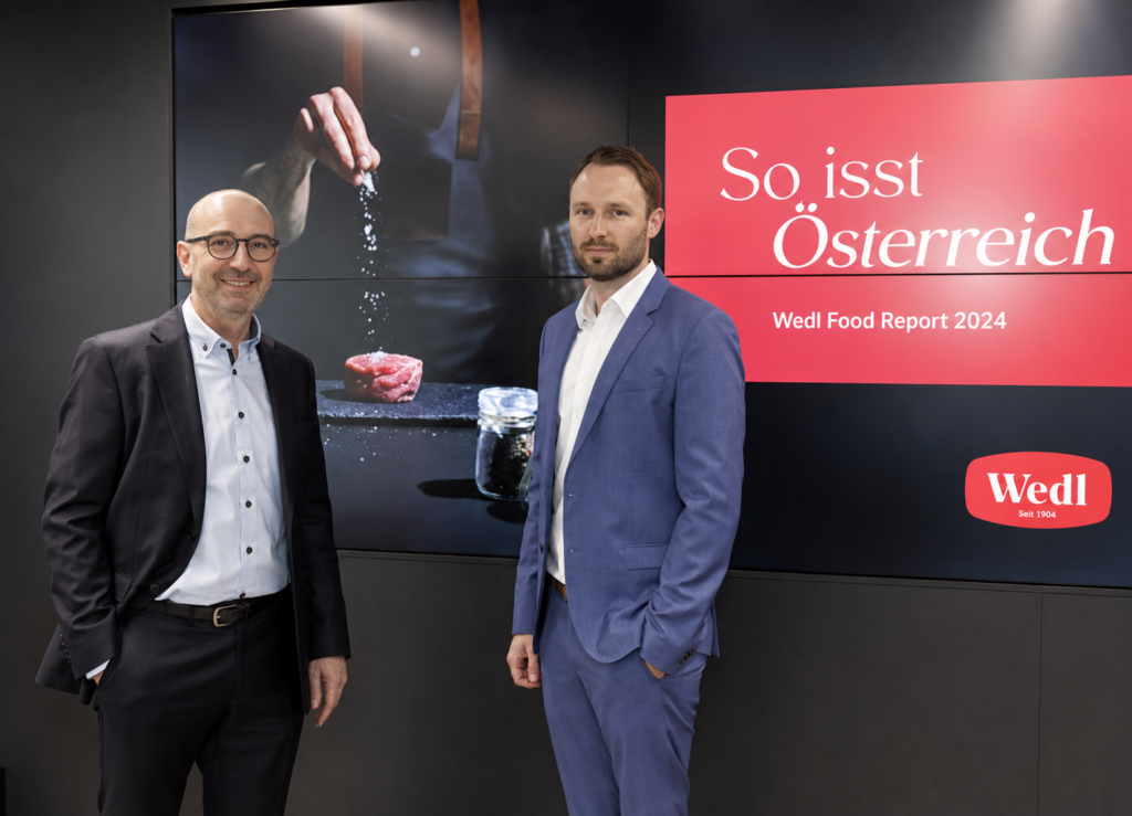 Zwei Männer in Anzügen stehen vor einem Bildschirm mit dem Wedl Food Report 2024.