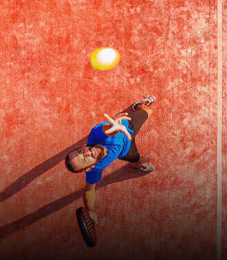 Ein Padel-Spieler auf rotem Platz blickt aus der Vogelperspektive nach oben zum Ball.
