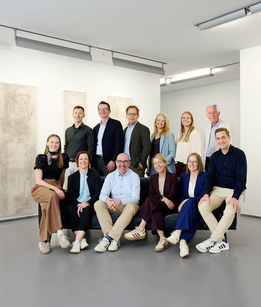 Ein lächelndes Team von Geschäftsleuten posiert gemeinsam in einem hellen, modernen Raum.