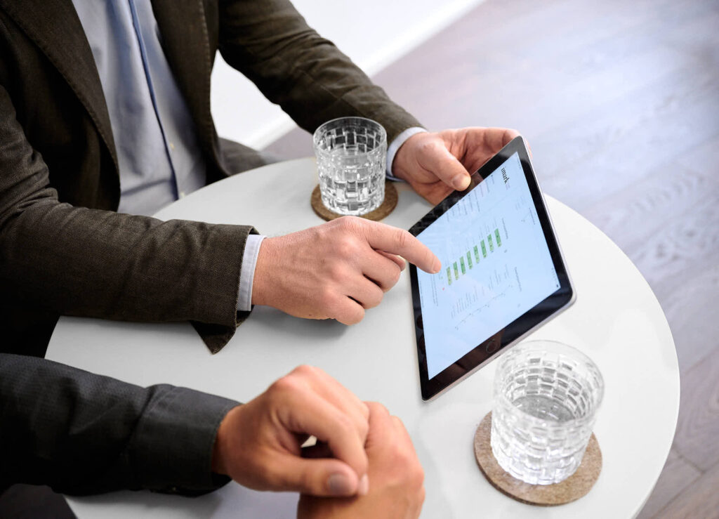 Ein Geschäftsmann zeigt auf ein Tablet mit Daten und Diagrammen am Tisch.