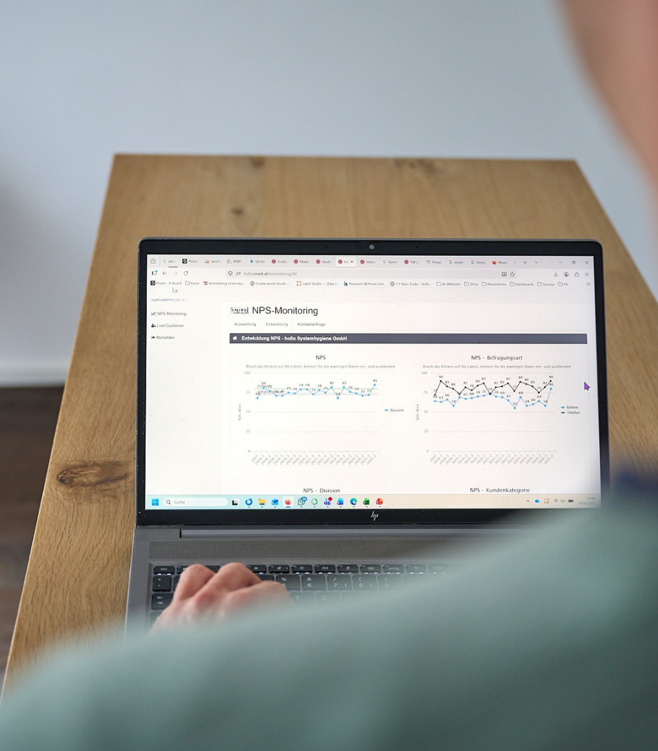 Eine Person arbeitet an einem Laptop mit NPS-Monitoring-Dashboard auf einem Holztisch.