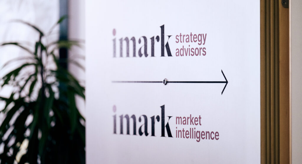 Weißes Wegweiserschild im Büro für imark strategy advisors und market intelligence mit Pfeil.