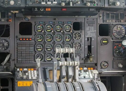 Instrumententafel eines Flugzeugcockpits mit vier zentralen Schubhebeln und analogen Instrumenten.