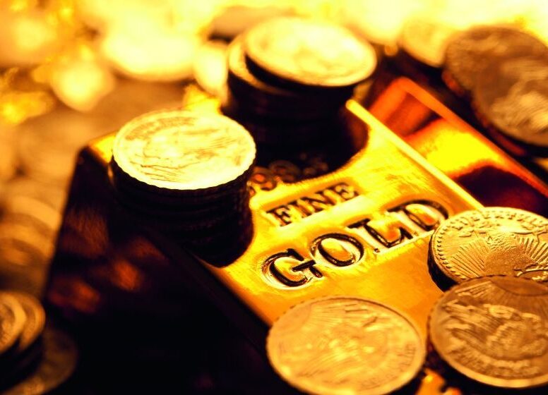 Glänzender Goldbarren mit der Prägung FINE GOLD umgeben von zahlreichen Goldmünzen.