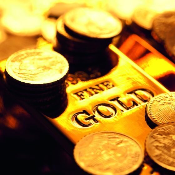Glänzender Goldbarren mit der Prägung FINE GOLD umgeben von zahlreichen Goldmünzen.