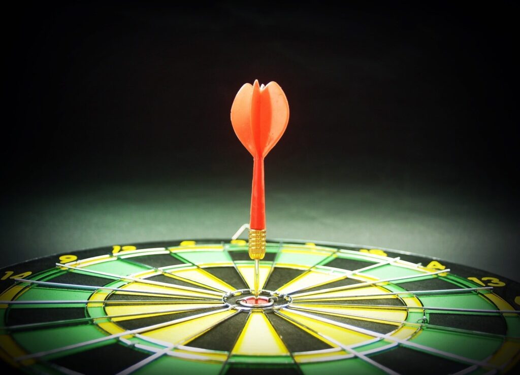 Ein roter Dartpfeil steckt direkt im Bullseye einer Dartscheibe.