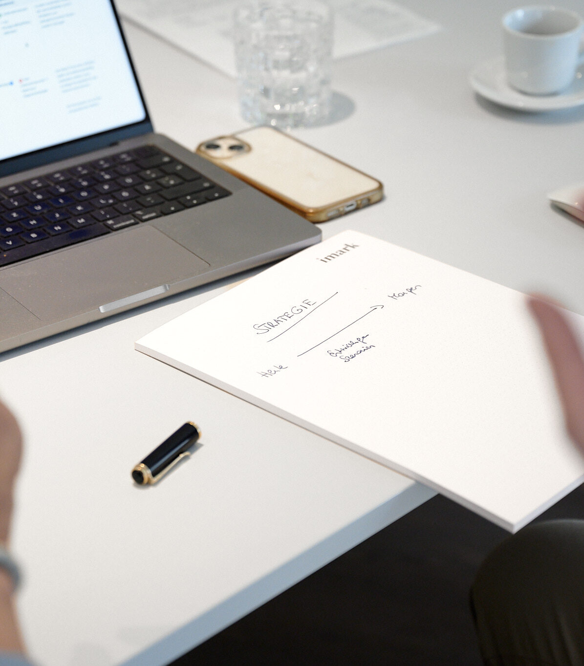 Moderner Arbeitsplatz mit Laptop, Smartphone und Notizblock mit handgeschriebener Strategie-Skizze.