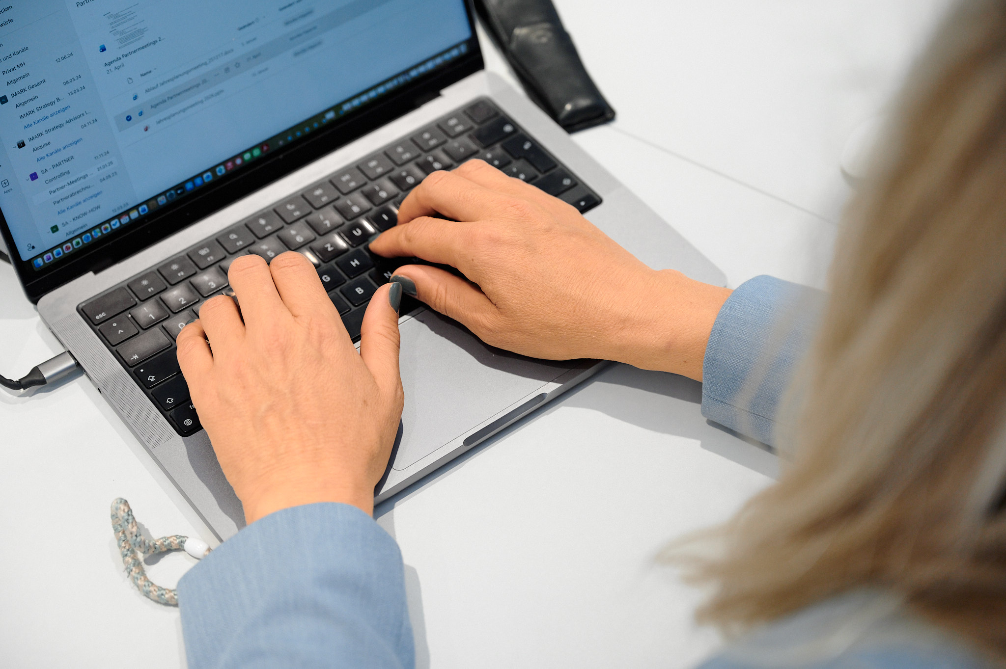 Hände einer Frau im blauen Blazer tippen auf der Tastatur eines silbernen Laptops.