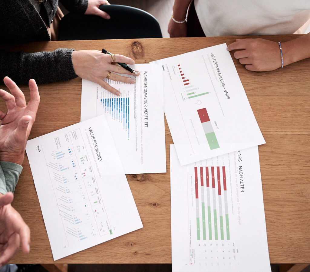 Personen analysieren ausgedruckte Berichte und Diagramme bei einem Meeting am Holztisch.