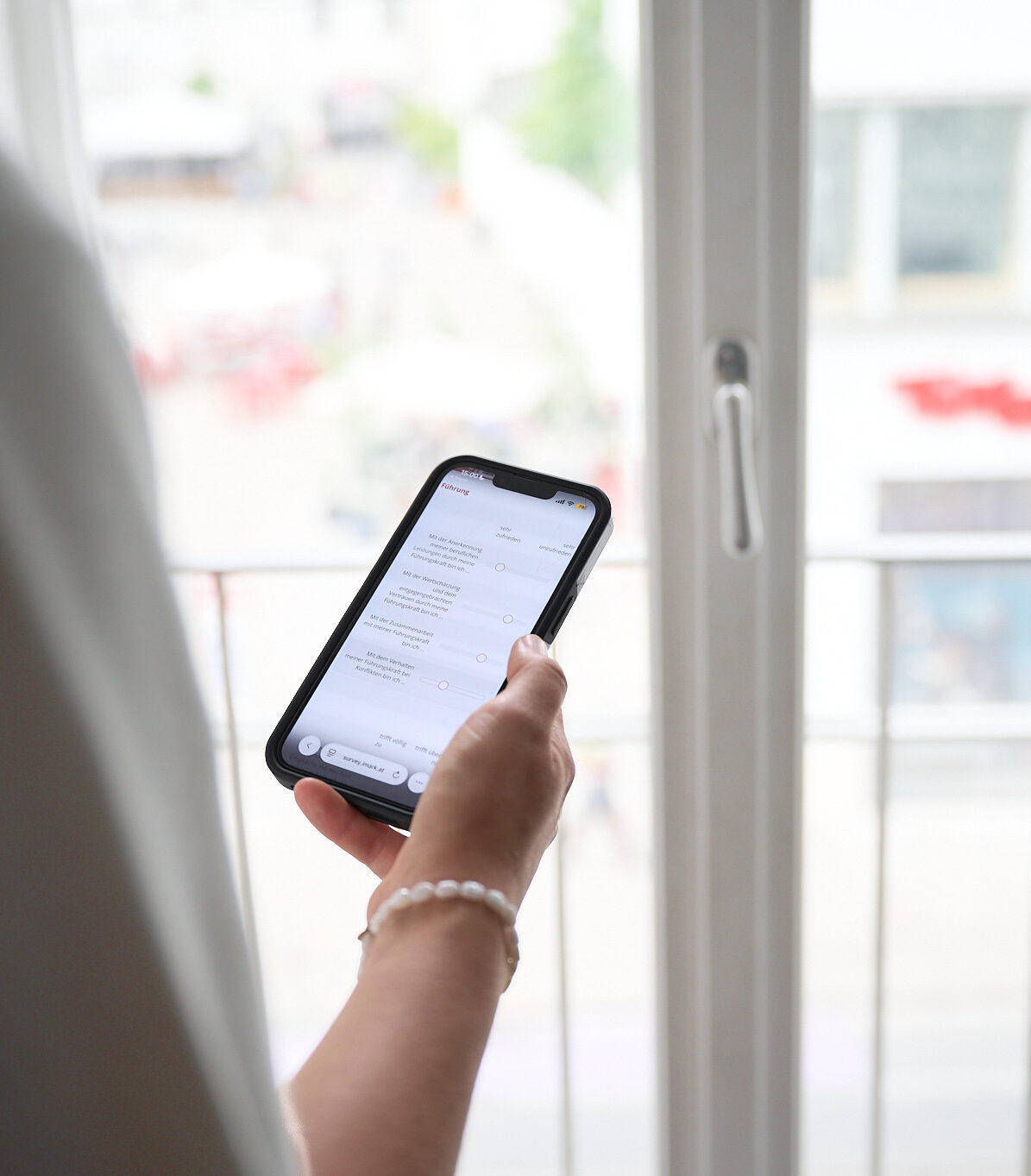 Eine Hand hält ein Smartphone mit einer Online-Umfrage vor einem hellen Fenster.