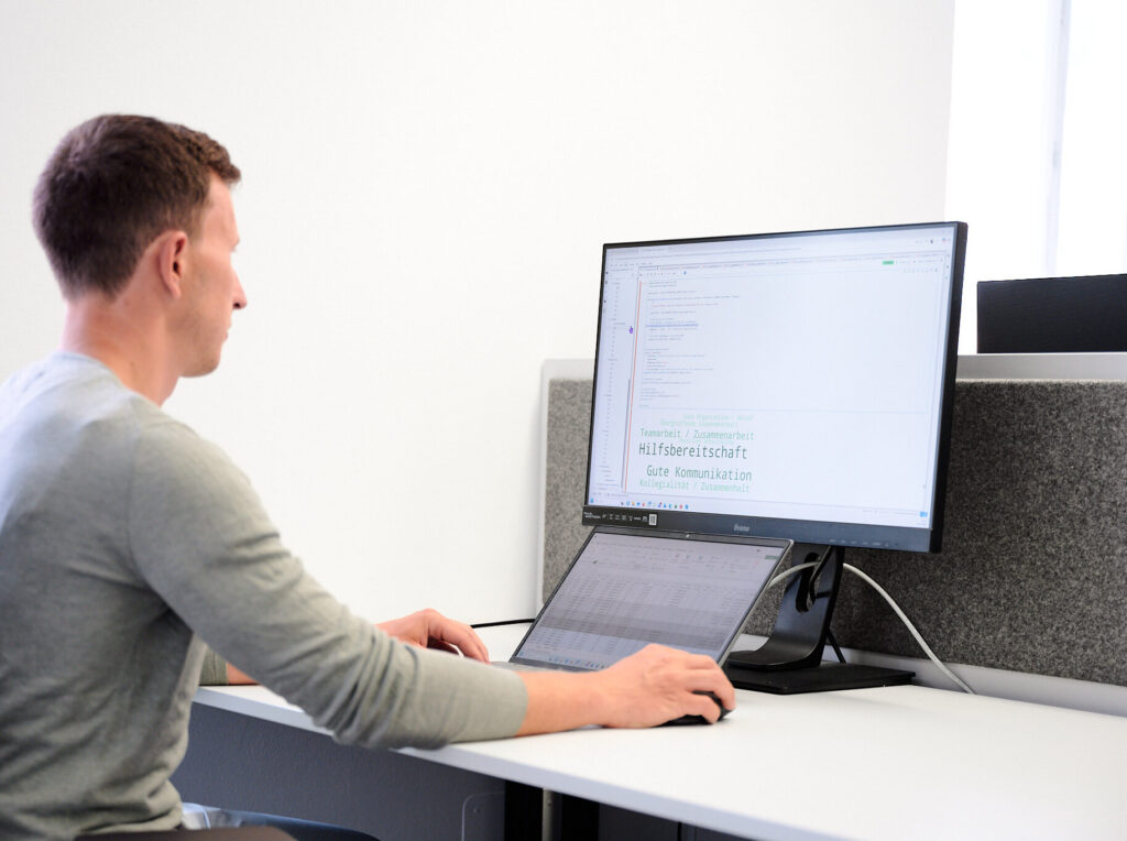 Ein Mann sitzt am Schreibtisch im Büro und arbeitet an einem großen Monitor.