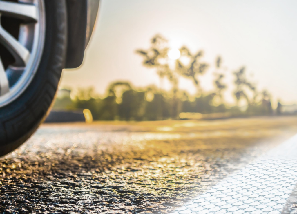 Nahaufnahme eines Autoreifens auf einer sonnenbeschienenen Asphaltstraße bei Sonnenuntergang.