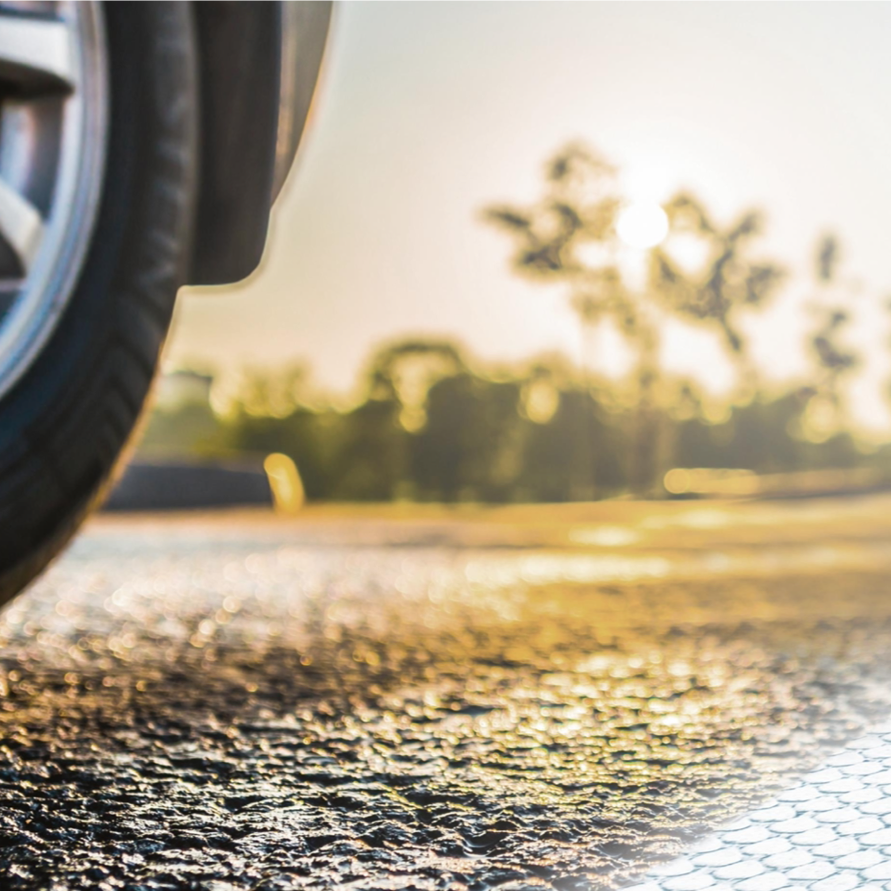 Nahaufnahme eines Autoreifens auf einer Asphaltstraße im warmen Licht der Abendsonne.