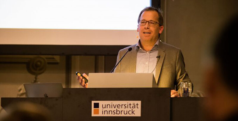 Ein Referent mit Brille hält einen Vortrag am Rednerpult der Universität Innsbruck.