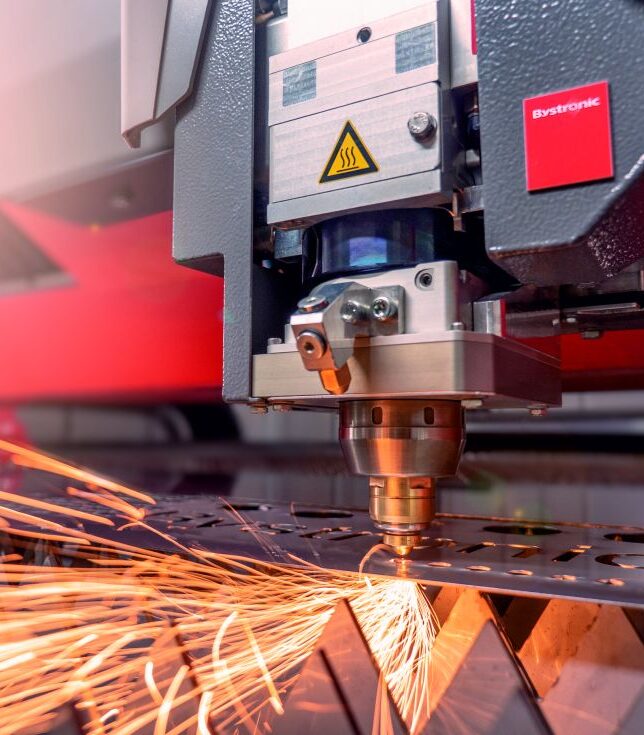 Ein industrieller Laserschneidkopf schneidet Metallblech unter starkem sprühendem Funkenflug.