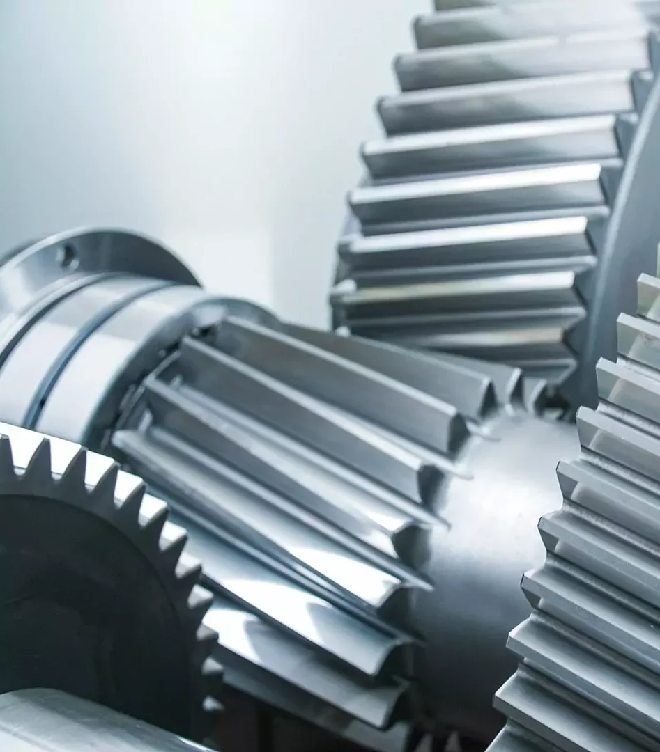 Große glänzende Metallzahnräder greifen präzise in einem industriellen Getriebe ineinander.