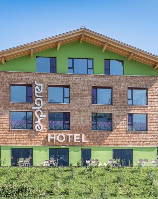 Moderne Fassade des Explorer Hotels mit Holzschindeln, grünen Akzenten und großen Fenstern.