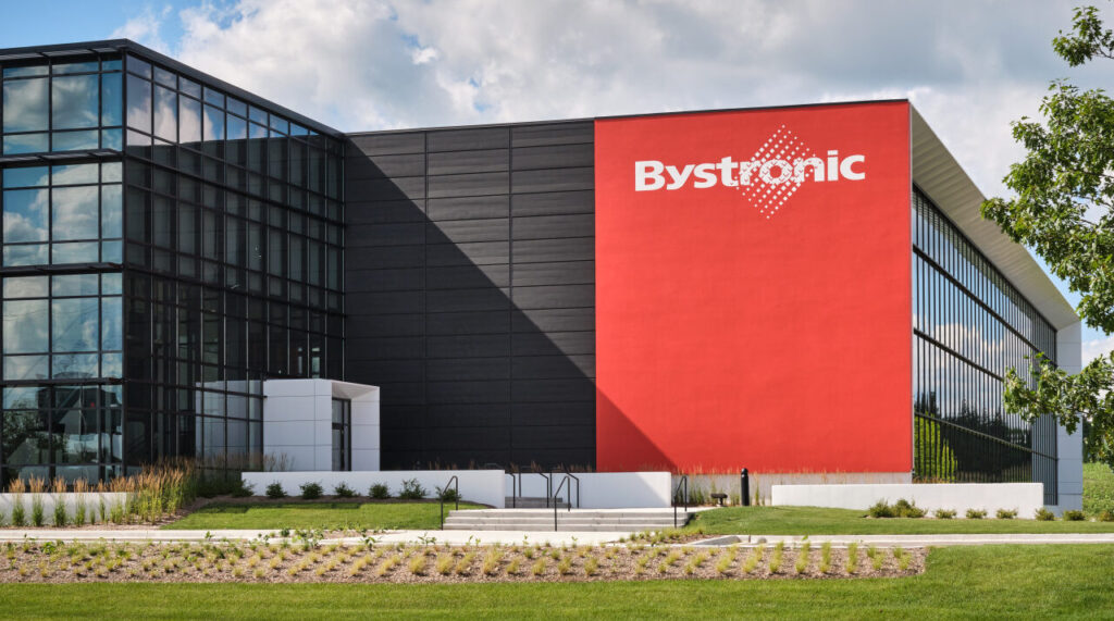 Modernes Bystronic-Firmengebäude mit roter Fassade, Glasfront und gepflegter Gartenanlage bei Sonnenschein.