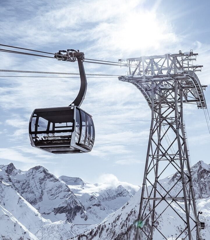 Eine moderne Seilbahngondel schwebt neben einer Stahlstütze über einer verschneiten Berglandschaft.