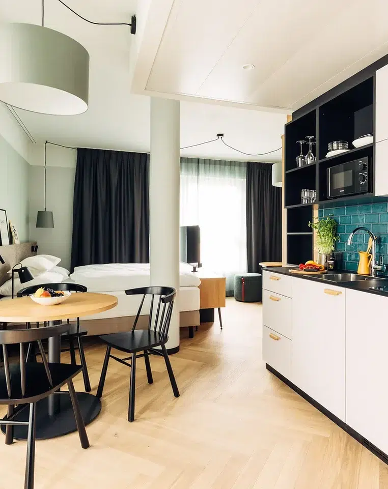 Modernes Studio-Apartment mit Küchenzeile, rundem Esstisch und Doppelbett im Hintergrund.