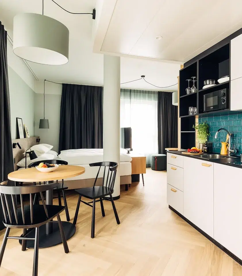 Modernes Studio-Apartment mit Küchenzeile, rundem Esstisch und Doppelbett im Hintergrund.
