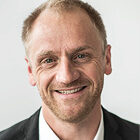 Ein freundlich lächelnder Mann im Anzug schaut direkt in die Kamera.
