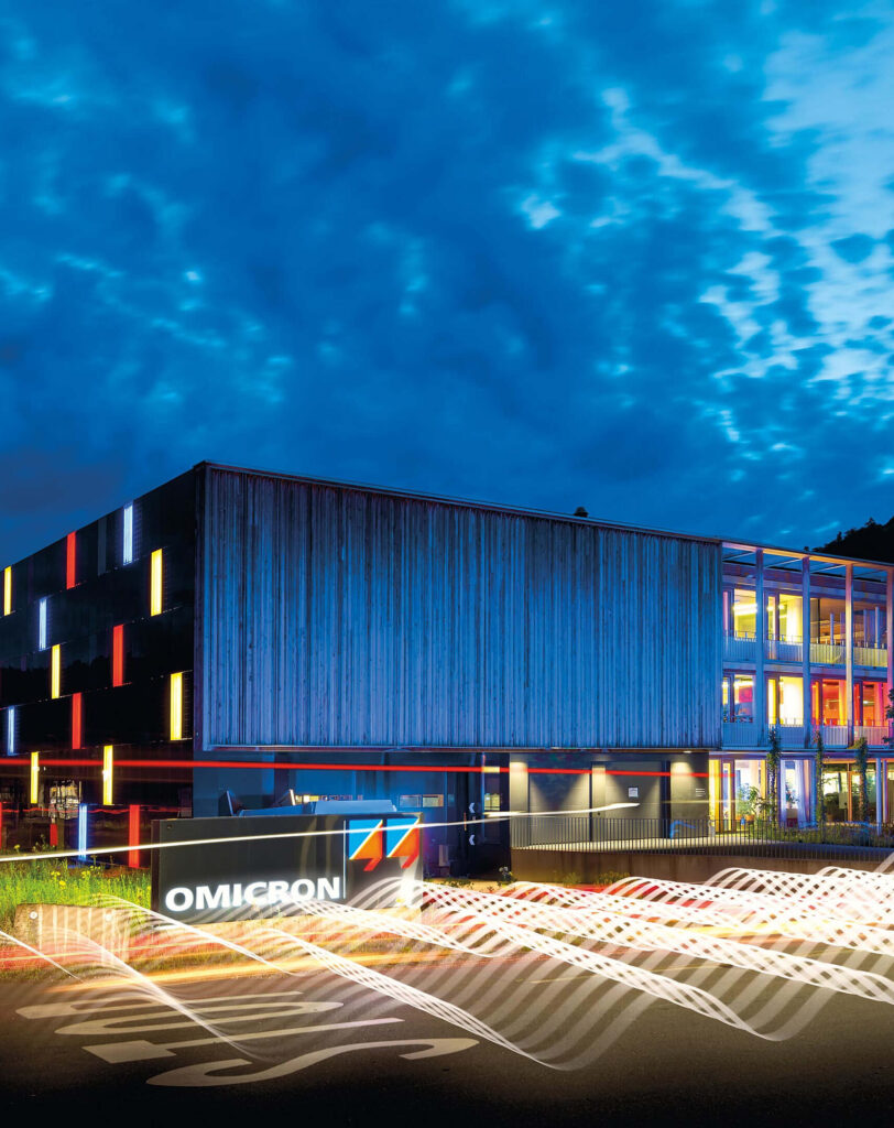 Beleuchtetes modernes Firmengebäude von Omicron bei Dämmerung mit bunten Lichteffekten.