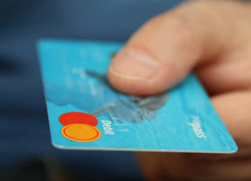 Eine Hand hält eine blaue Debitkarte für eine kontaktlose Bezahlung.