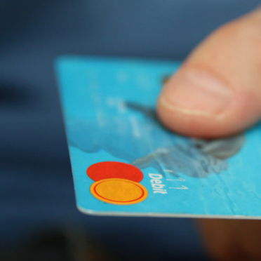 Ein Daumen hält eine blaue Debitkarte mit rot-gelbem Logo.